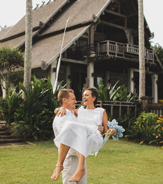 A newly married couple laughs on the lawn of a resort while the groom carries the bride.