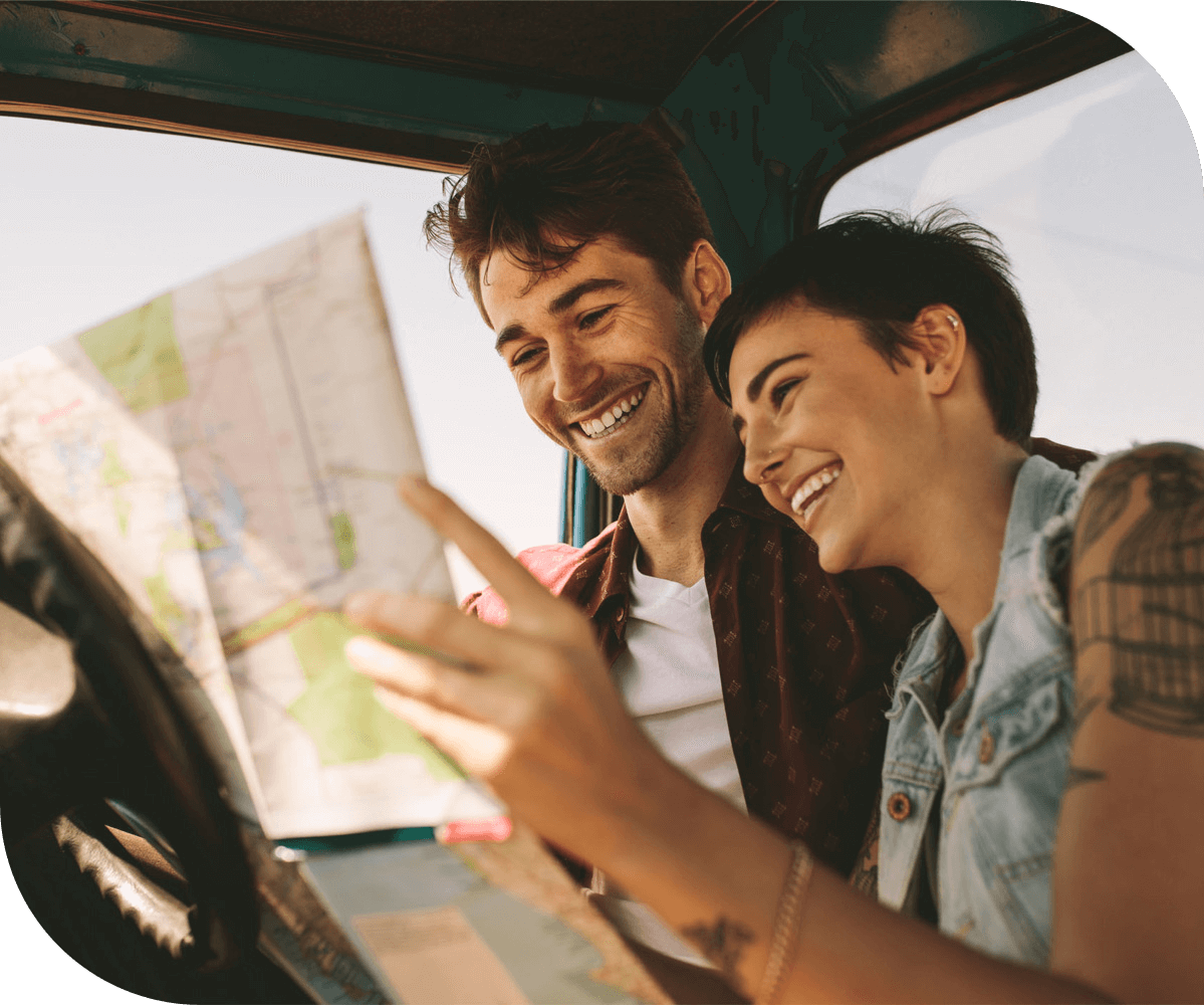 a couple on a road trip are laughing together while they look at a paper map