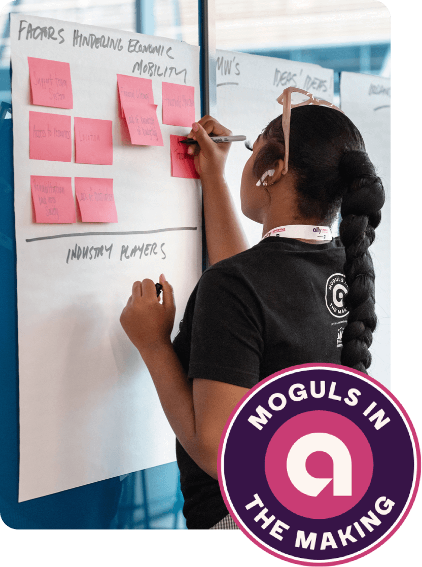 An HBCU student with a long, braided ponytail writes ideas on a wall of sticky notes.
