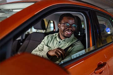 Man smiles as his sits in the drivers seat of his new car.