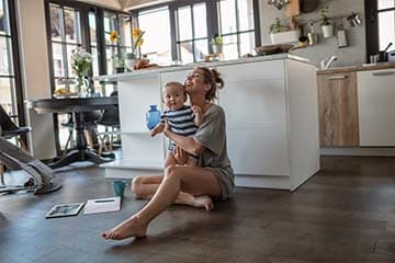 A woman is sitting on the floor in her kitchen playing with her baby.