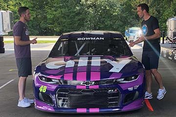 Alex Bowman and Christian Fuchs standing on either side of Ally-wrapped NASCAR car
