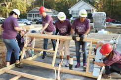 Five Ally volunteers wearing hard hats and purple Ally shirts helping build a home for Habitat for Humanity