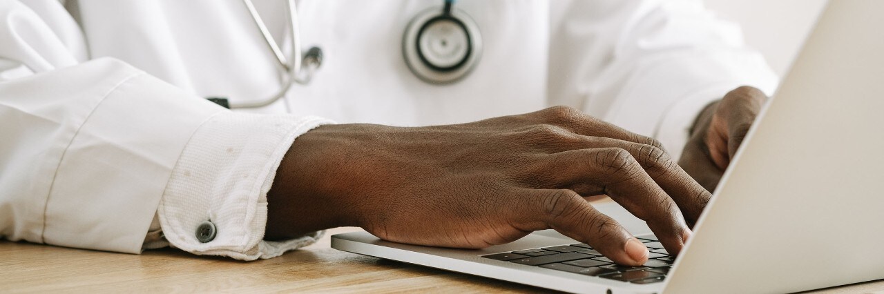 Hands of a black male doctor typing on a laptop