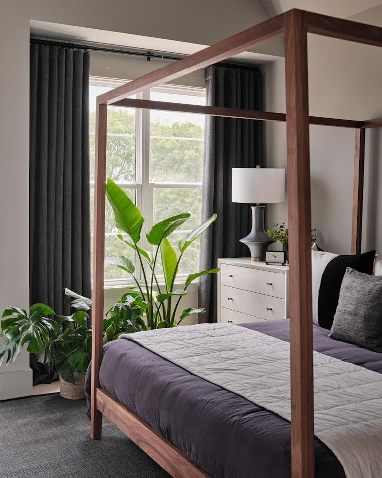 A bedroom with plants by the window. The curtains are open and letting sunshine inside the room.