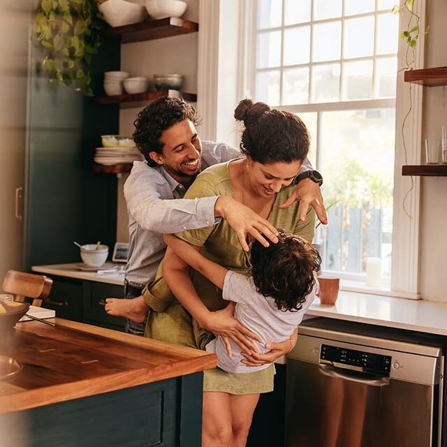 A mother and father are playing with their child in the kitchen of their home.