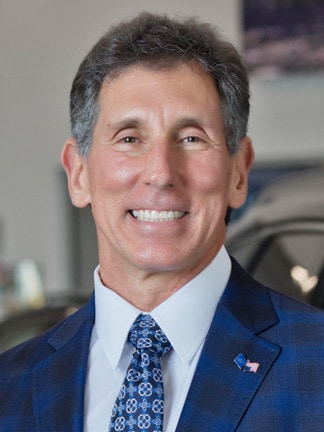 Headshot of Gary Rome, a white man with dark brownish, gray hair wearing blue plaid suit jacket, white button-down shirt, and blue design tie. 