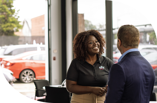 a smiling female Ally employee shaking the hand of a dealer at a dealership