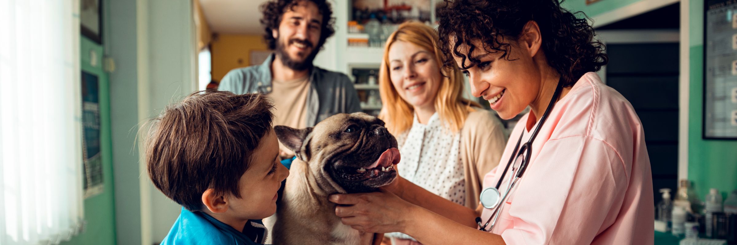 a smiling Veterinarian playing with a tan Pug dog while surrounded by a happy family of three