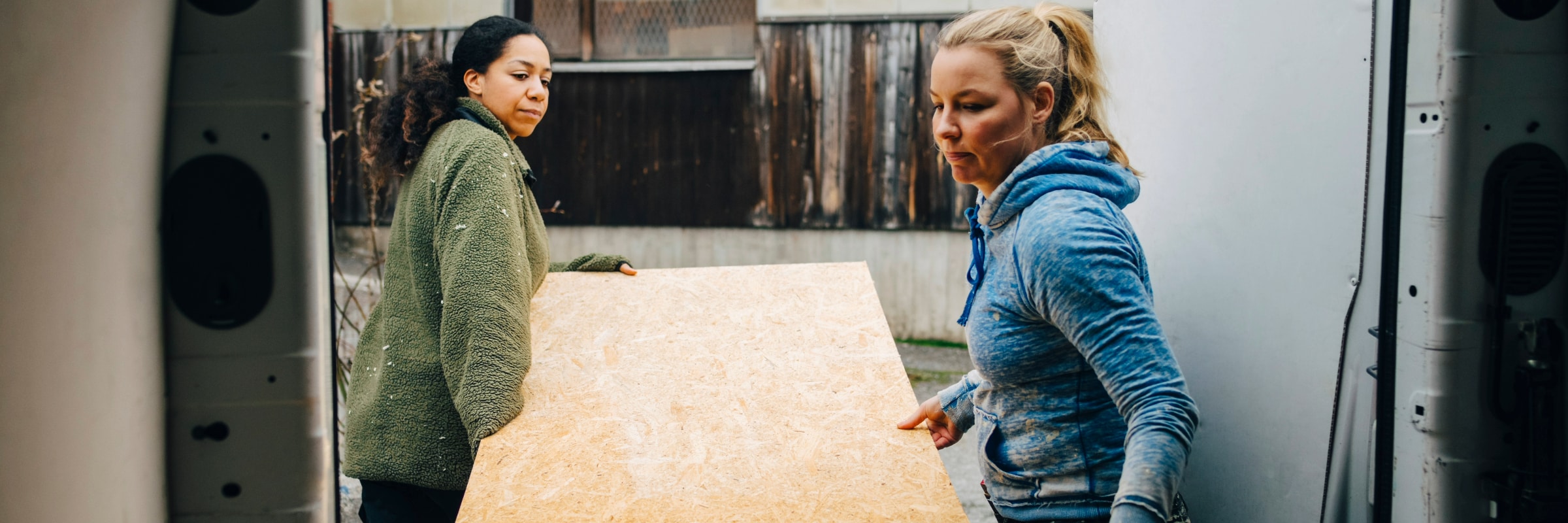 Two female carpenters load a wooden board into the back of a van