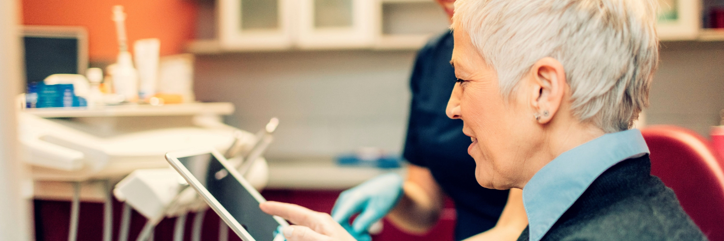 Mature woman speaks with her dentist who is holding a digital tablet
