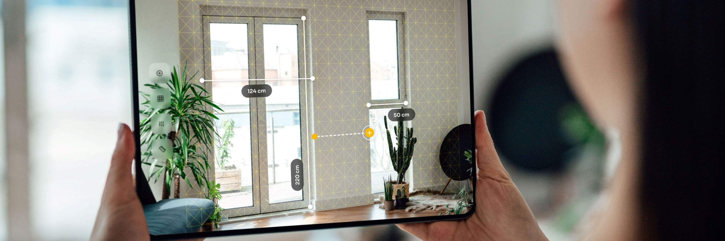 Over the shoulder view of young woman using Augmented Reality technology to measure dimensions of home interior on digital tablet.
