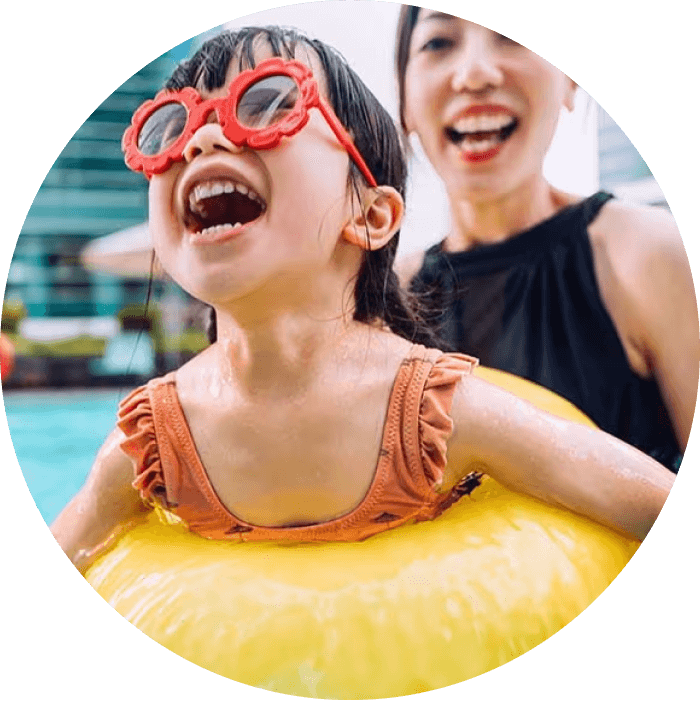 A young child with oversized sunglasses joyfully swims with a floatie.