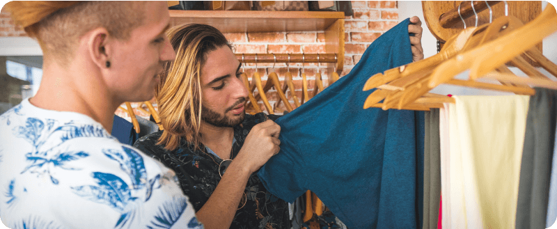 Man with long, bleached hair peruses clothing on hangers.