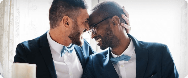 Two men at a formal event put their foreheads together, smiling.