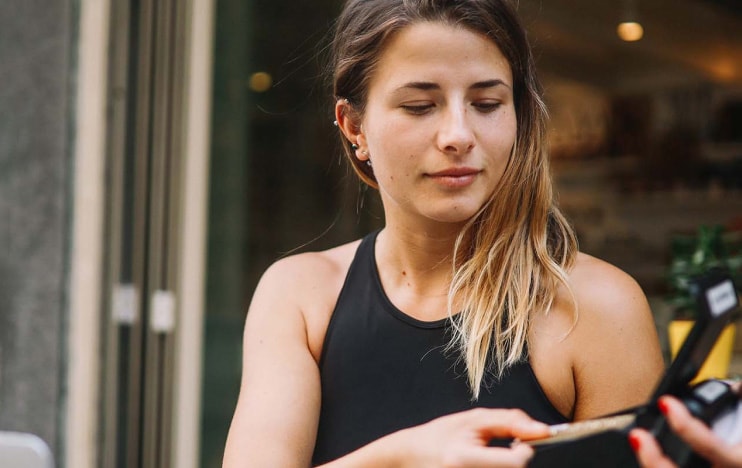Young woman sitting at a table at a cafe pays for her coffee