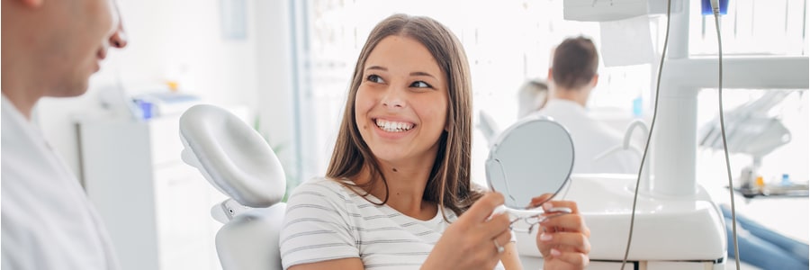 Woman holding a mirror and smiling in dentist office.