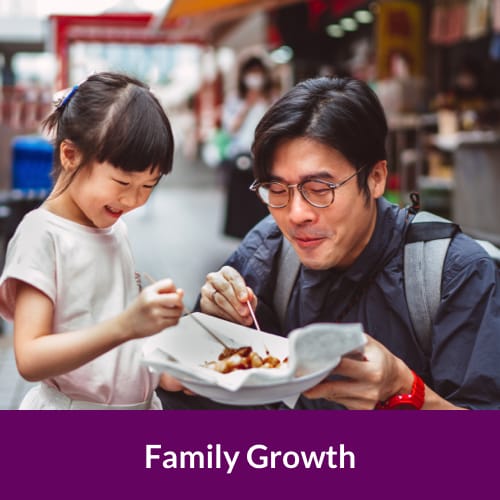 a father kneeling down holding a plate of food and sharing it with his smiling toddler daughter