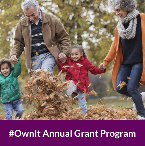 an older man and woman holding hands with their grandson and granddaughter as they leap through a pile of brown leaves on an autumn day