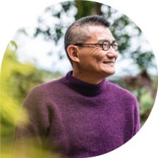 Middle-aged Asian man wearing black-framed glasses and a purple turtleneck sweater