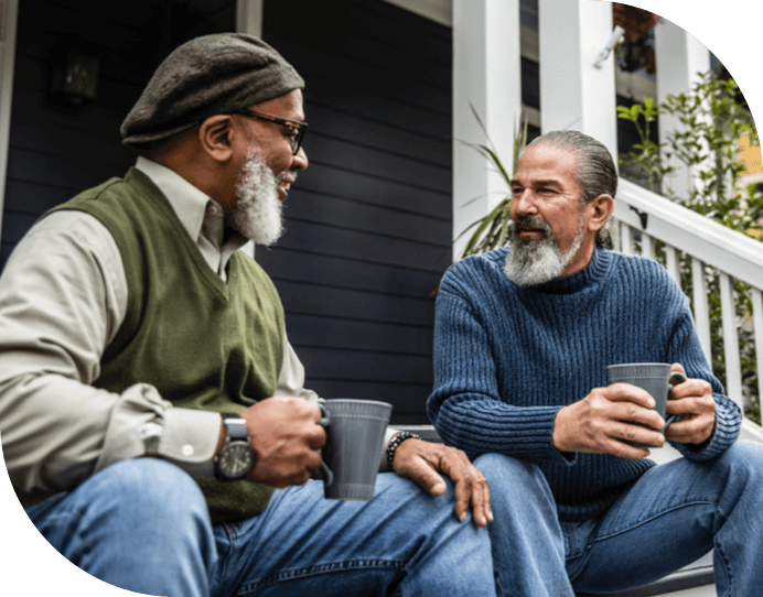Two middle aged men sitting on front porch steps chatting and drinking coffee
