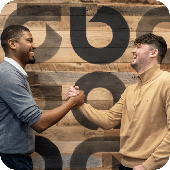 Two Ally employees enthusiastically greeting each other with a handshake.