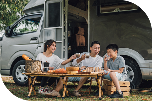 mother and father with young son seated at a table outside a camper van
