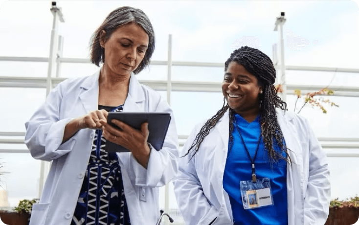 Two women in white coats look at a tablet together