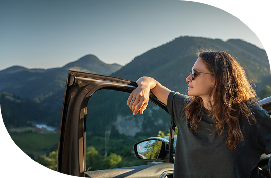 a woman standing inside the driver’s side door of her vehicle gazing at the mountains.