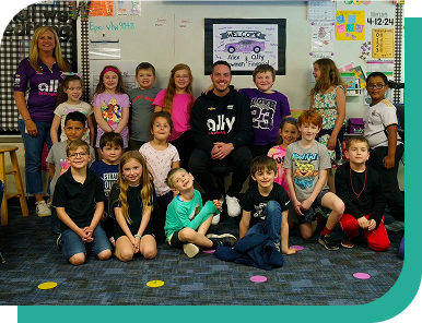 NASCAR driver Alex Bowman sits in an elementary school classroom in the middle of a group of kids.