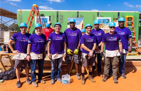 a group of male and female Ally employees wearing hardhats and volunteering at a building site