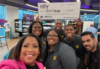 a group of young male and female college students posing with a check presented to them by Ally employees.