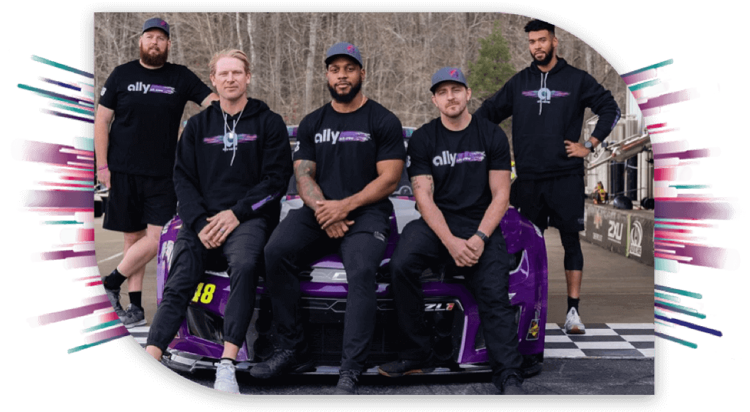 Five members of the Ally pit crew pose with the No. 48 car while wearing this year's new gear: black shirts with the logo and colorful starburst lines, and gray hats with the Ally Racing logo - a multicolored Ally "a".