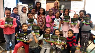 Group of children holding an Ally book with a teacher in a classroom