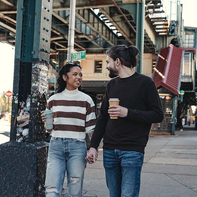 Couple walking down city street together with coffees in hand