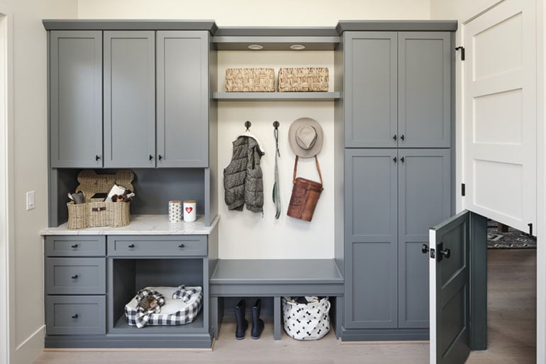 Photo shows cabinetry in a mudroom with a Dutch door to allow pets easy access. Items like a hat and vest hang on the wall.