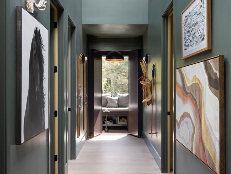 A hallway with artwork on both sides leads to a reading room with a large, sunny window.