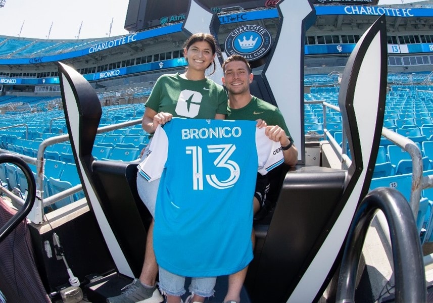 Brandt Bronico and his wife sit on Charlotte FC throne in the stadium holding a Bronico jersey