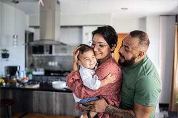 A happy family of three embrace in a modern kitchen.