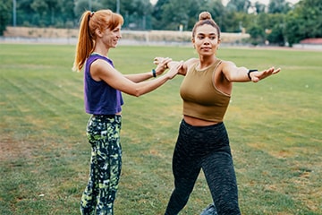 One woman guides another in a yoga practice on an athletic field