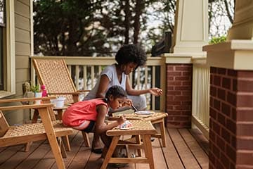 Mother and daughter paint while sitting in chairs on the front porch of their home.