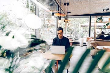 Young millennial on his laptop at a mid-century modern coffee shop considering his DIY investment options