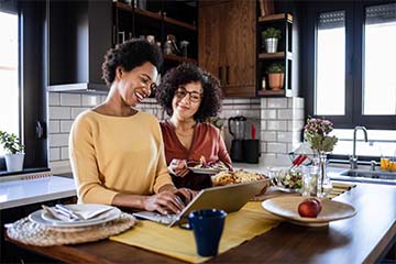 Two women stand at the kitchen counter on a laptop