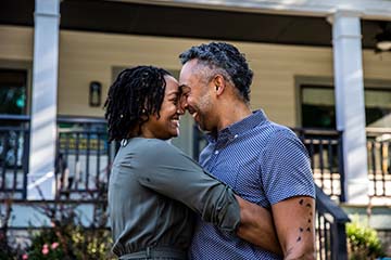 Husband and wife embracing in front of home. 