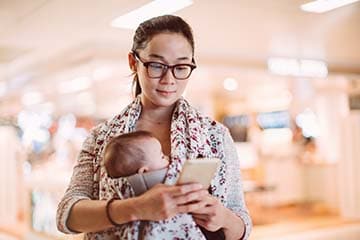 Young woman checks her phone while carrying a baby strapped in a front carrier
