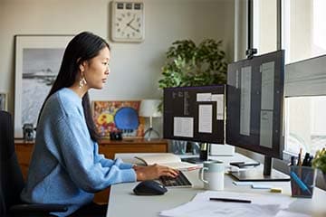 Woman sitting at desk working on multiple computer screens