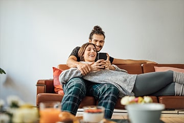 Couple sitting on couch together laughing while looking at phone