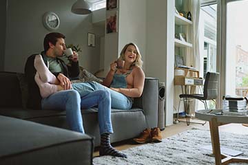 A happy couple sitting on the couch in their living room drinking coffee