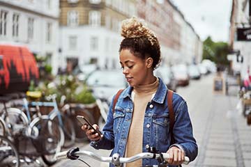 Woman on a city street walking a bike while checking her smart phone