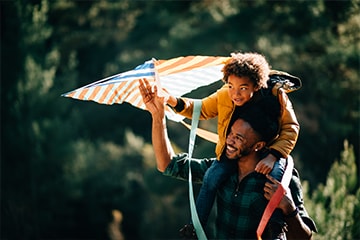 Young boy flying a kite while sitting on his father's shoulders